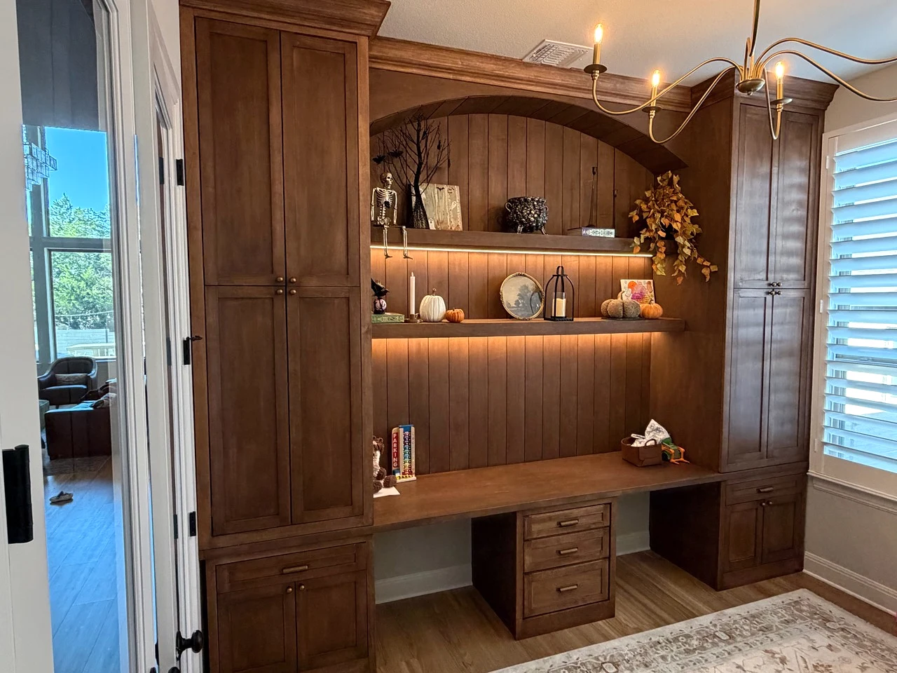 Completed study built-in with tall wood cabinets, a fitted desk, and illuminated shelves